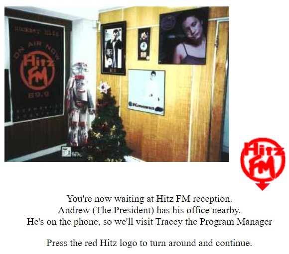 A screenshot of a Hitz FM virtual tour on the Raw Wild Hitz Connection website.  The photo shows a corner of the reception area in their St Kilda Road studios. There's multiple music posters on the wall, and a Christmas tree.